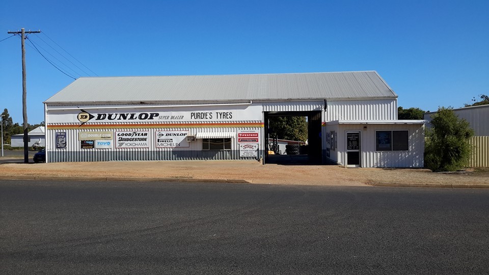The Purdie's Tyres shed in its earlier white paint, with the Dunlop Super Dealer sign and tyre brand boards along the front