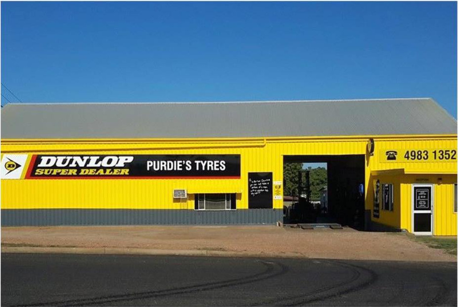 The Purdie's Tyres shed painted yellow, with the phone number in large figures beside the workshop door