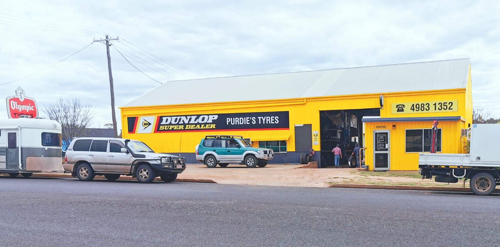 Vehicles and a horse float parked outside Purdie's Tyres while two people work in the open workshop bay